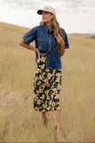 Woman in a denim jacket and floral dress standing in a field