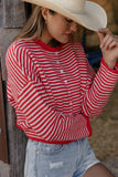Woman wearing a red and white striped shirt and a wide-brimmed hat, standing against a wooden wall.