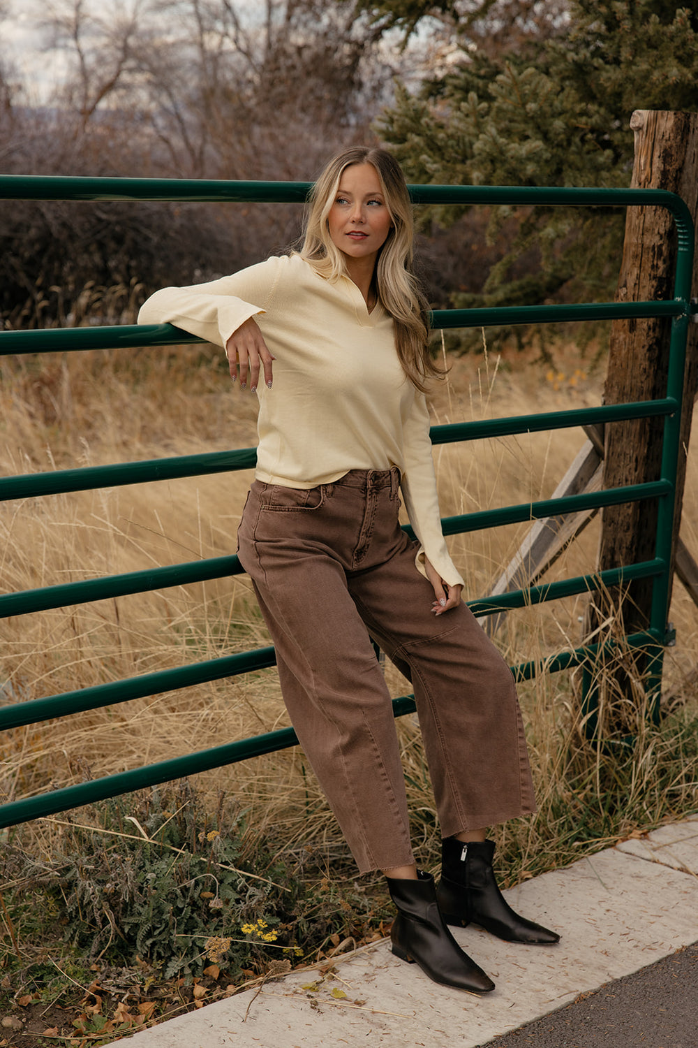 Woman standing by a green metal gate in a natural setting