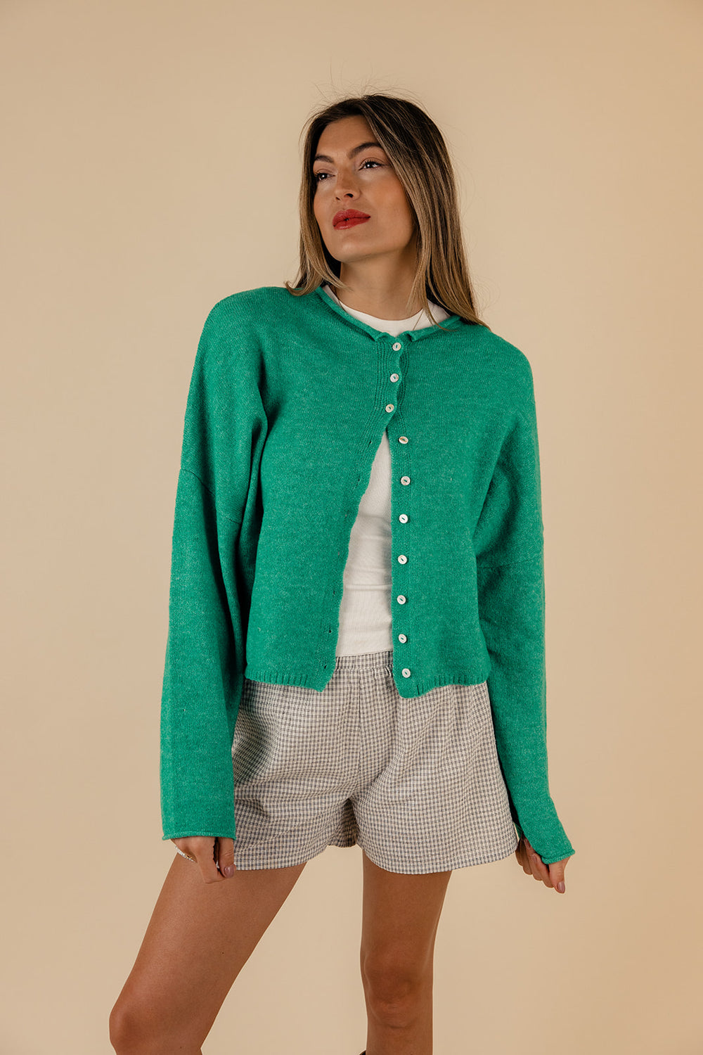 A woman wearing a green button-up cardigan with a rolled collar and arm cuffs, paired with light gray shorts.