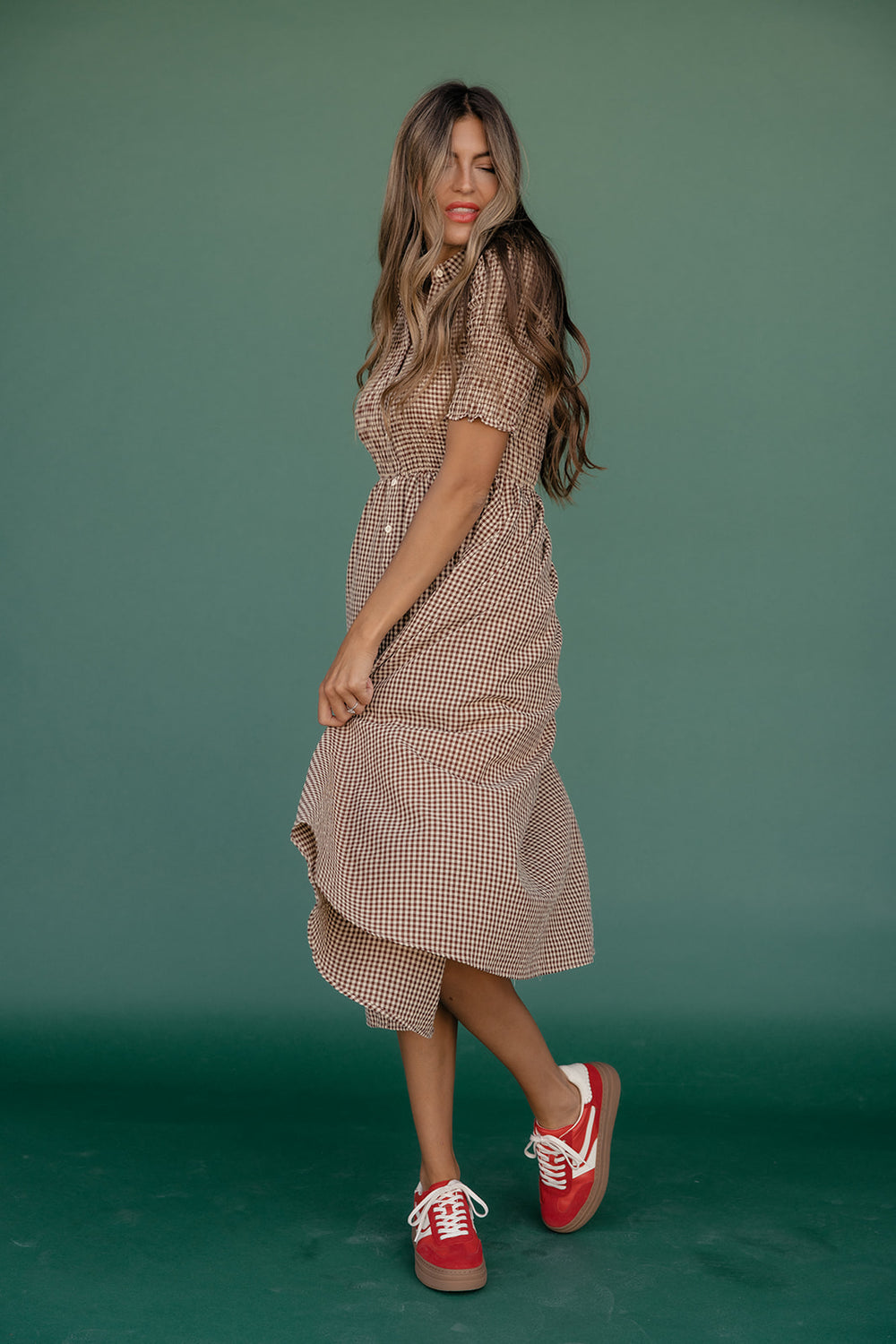 Woman wearing a checkered dress and red sneakers against a green background