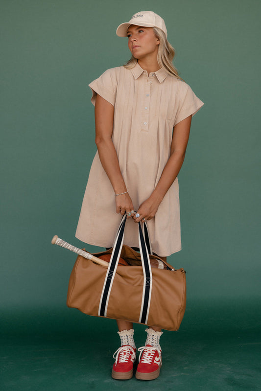 Woman in a beige dress holding a brown bag against a green background