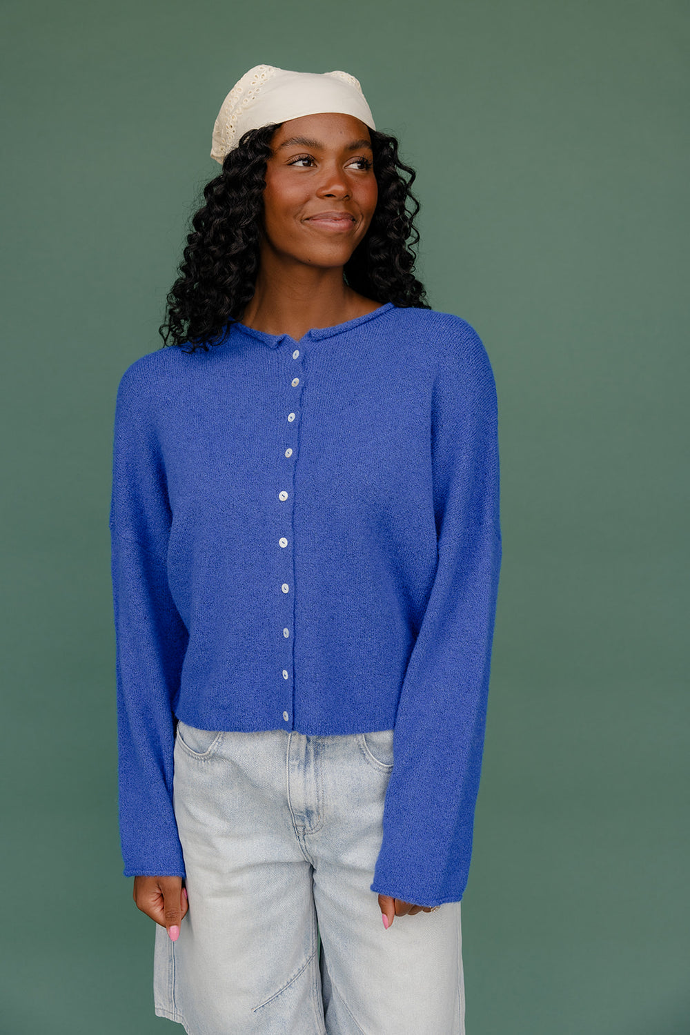 Woman wearing a blue cardigan and light-colored pants against a green background