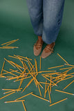 Person wearing blue jeans and brown shoes standing on a green floor with scattered yellow pencils.