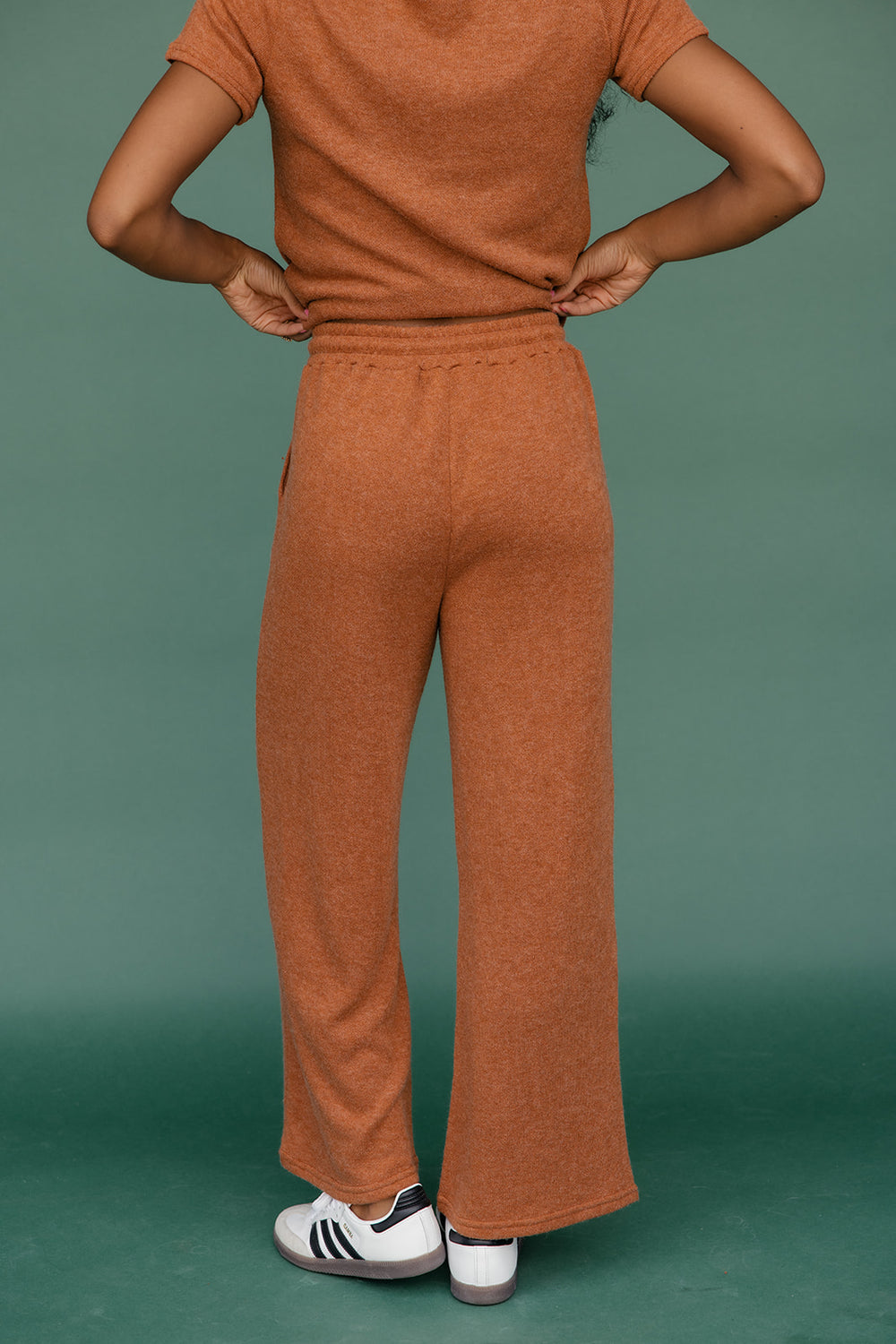 Person wearing a brown outfit with wide-leg pants against a green background