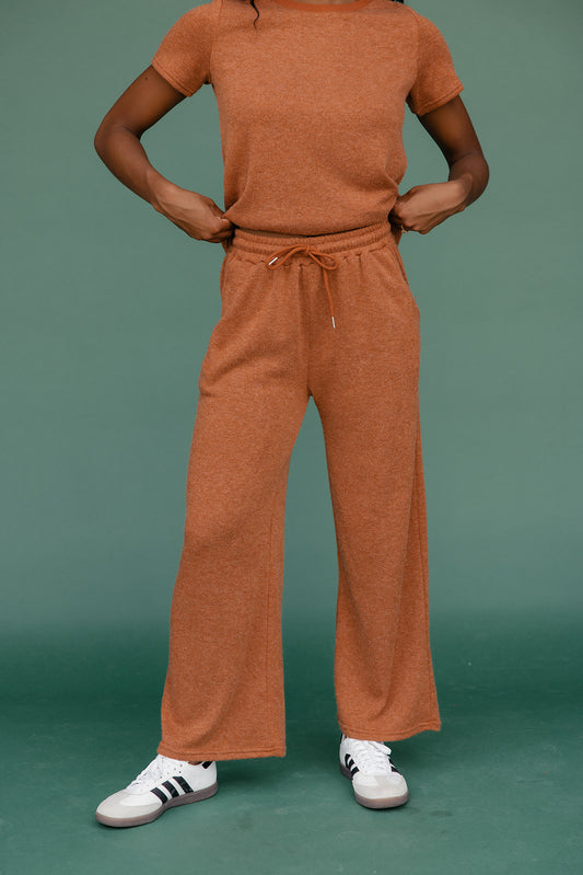 Person wearing a brown outfit with white sneakers on a green background