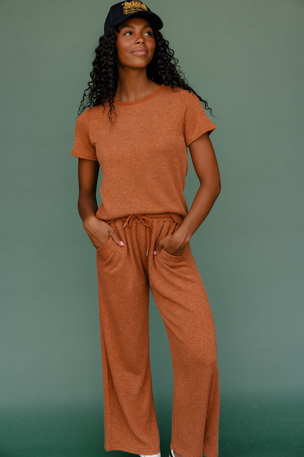 Woman wearing a brown outfit with a black cap against a green background