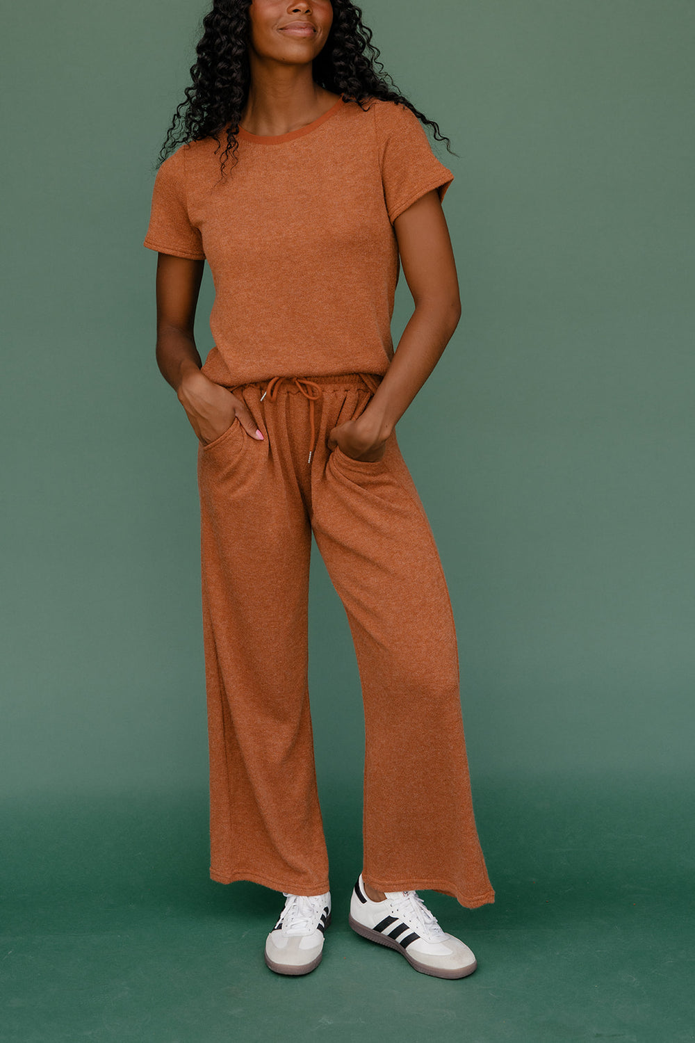 Person wearing a brown outfit with white sneakers on a green background