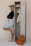 Person standing next to an open locker with clothes and a backpack on a plain background