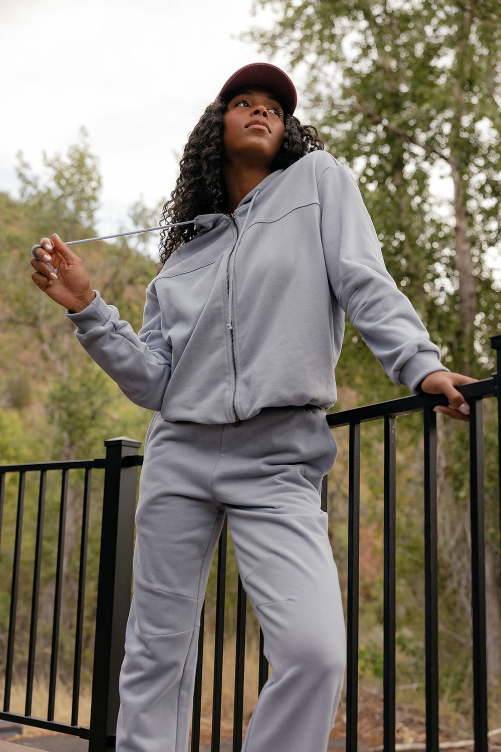 Woman in a gray tracksuit standing outdoors with trees in the background