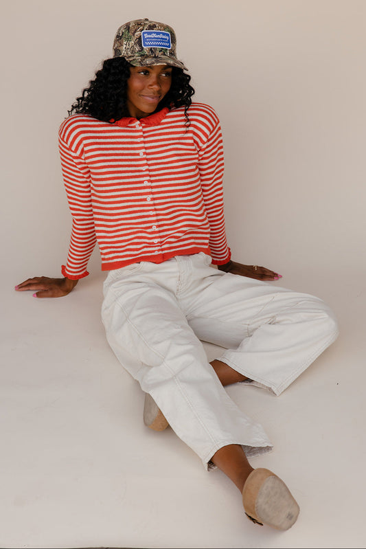 Person wearing a red and white striped shirt and white pants sitting on a white surface.
