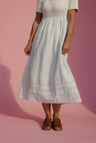 Person wearing a light blue skirt and white top on a pink background