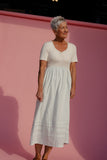 Woman in a white dress standing against a pink wall