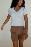 Woman wearing a light blue shirt and brown shorts against a plain background