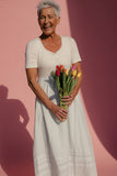 Woman in a white dress holding flowers against a pink background