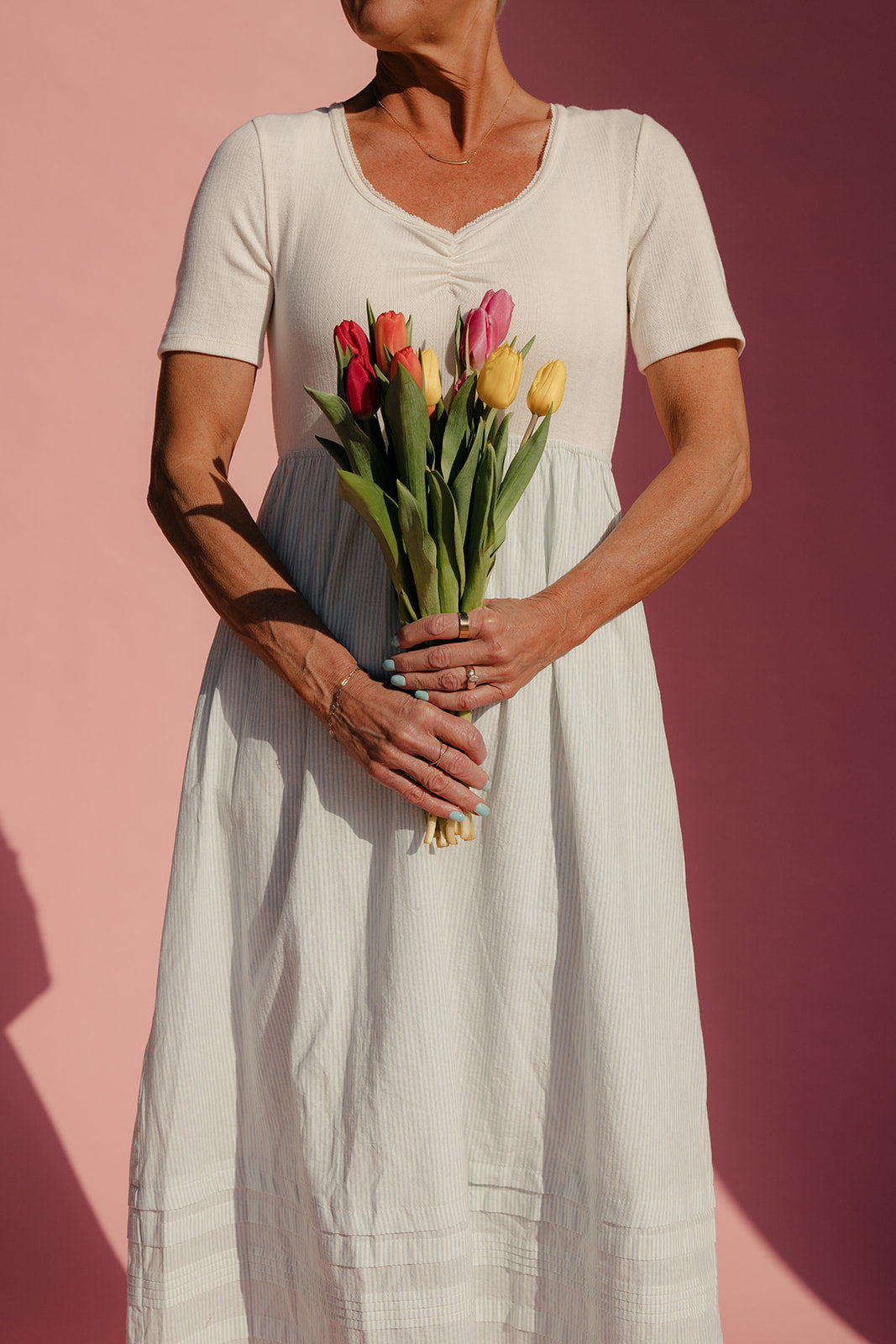 Woman holding a bouquet of tulips against a pink background