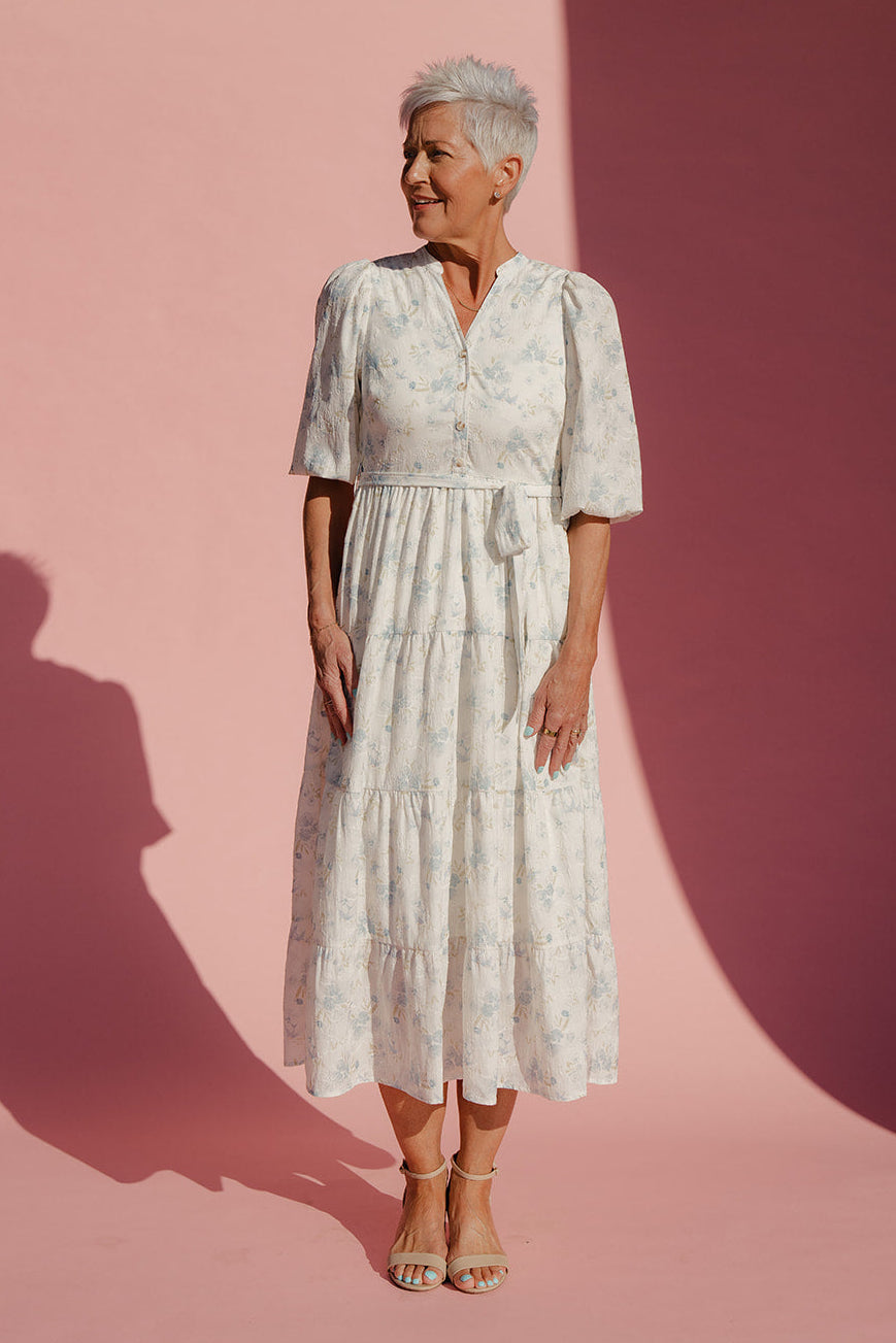 Woman in a white dress standing against a pink and purple gradient background