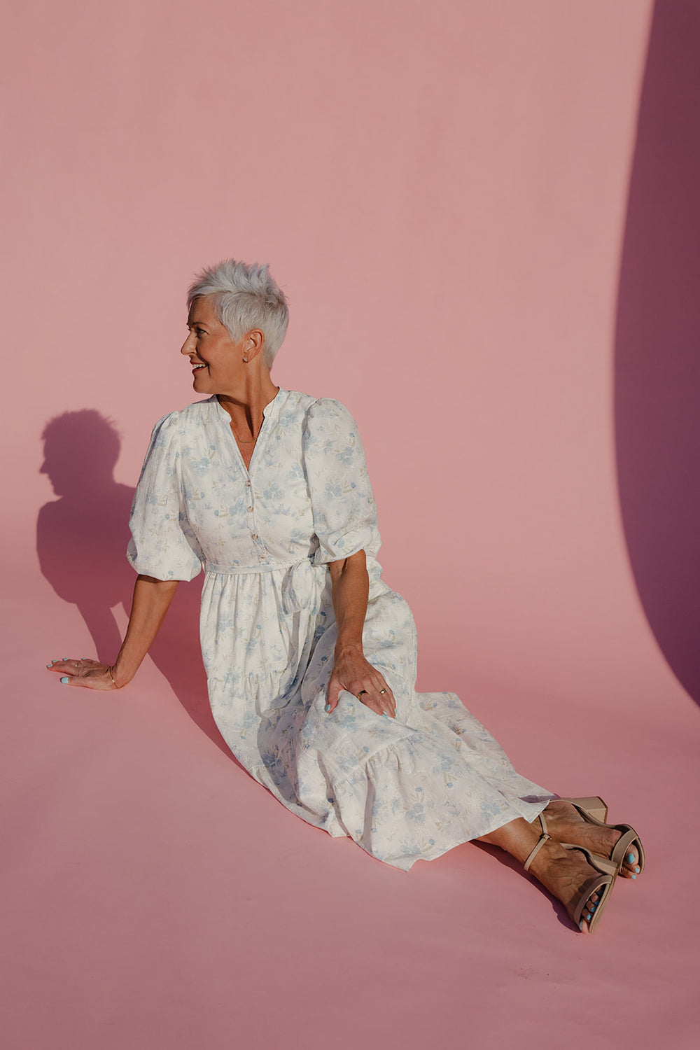 Woman in a white floral dress sitting on a pink background