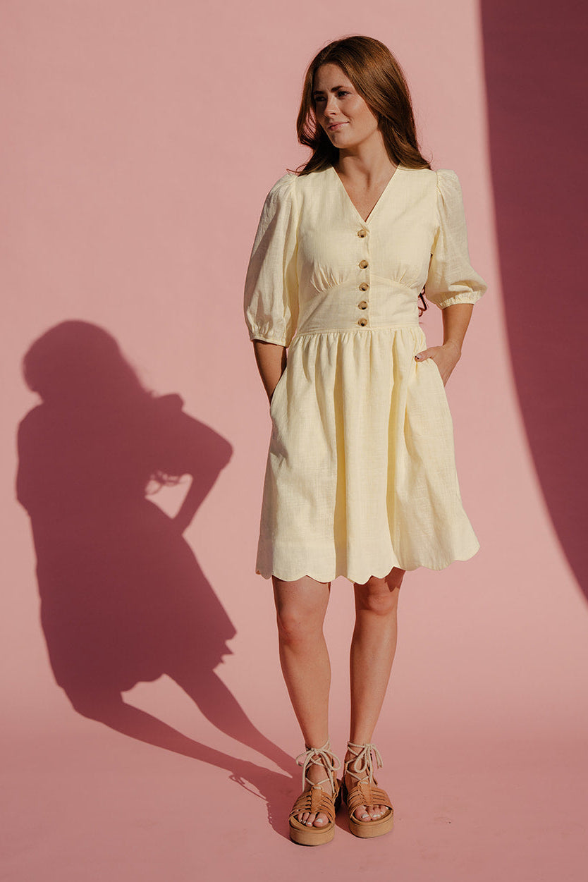 Woman in a light yellow dress standing against a pink background