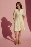 Woman in a light yellow dress standing against a pink background
