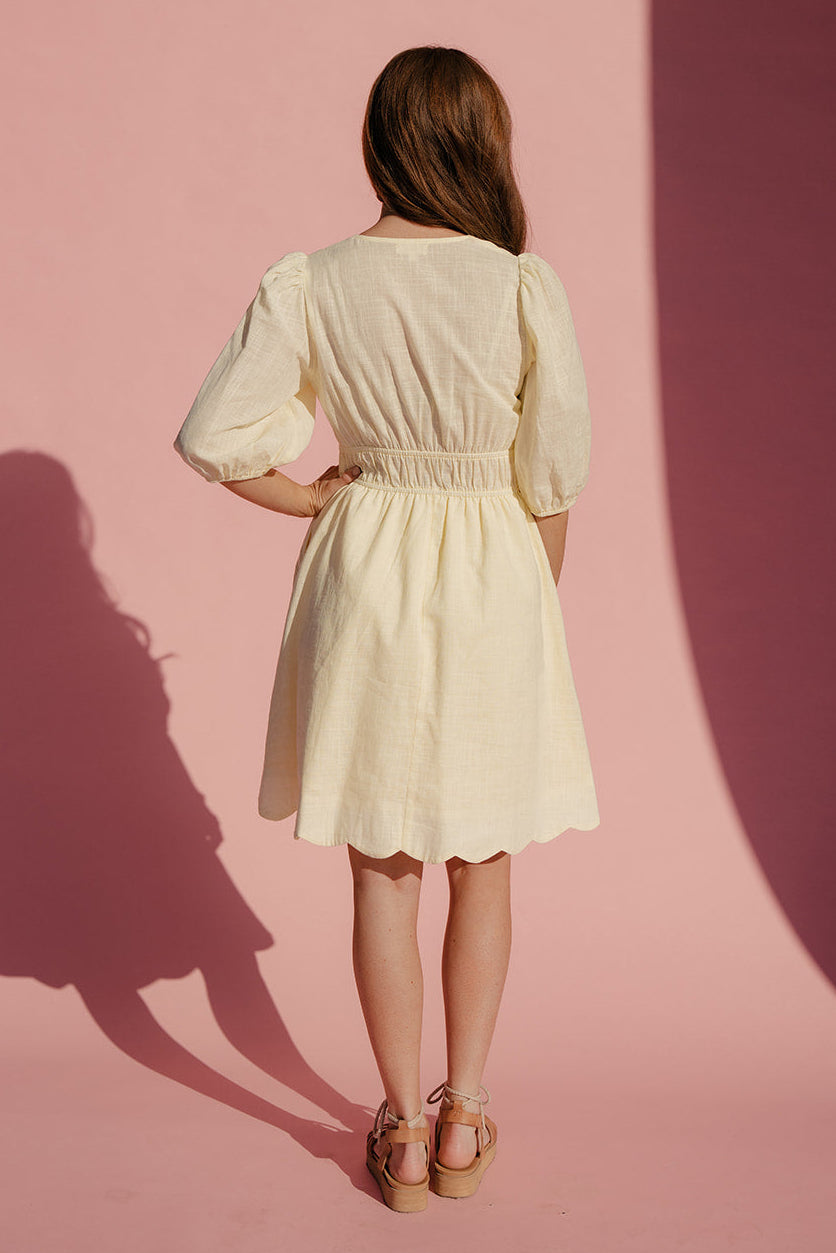 Woman in a light yellow dress standing against a pink background