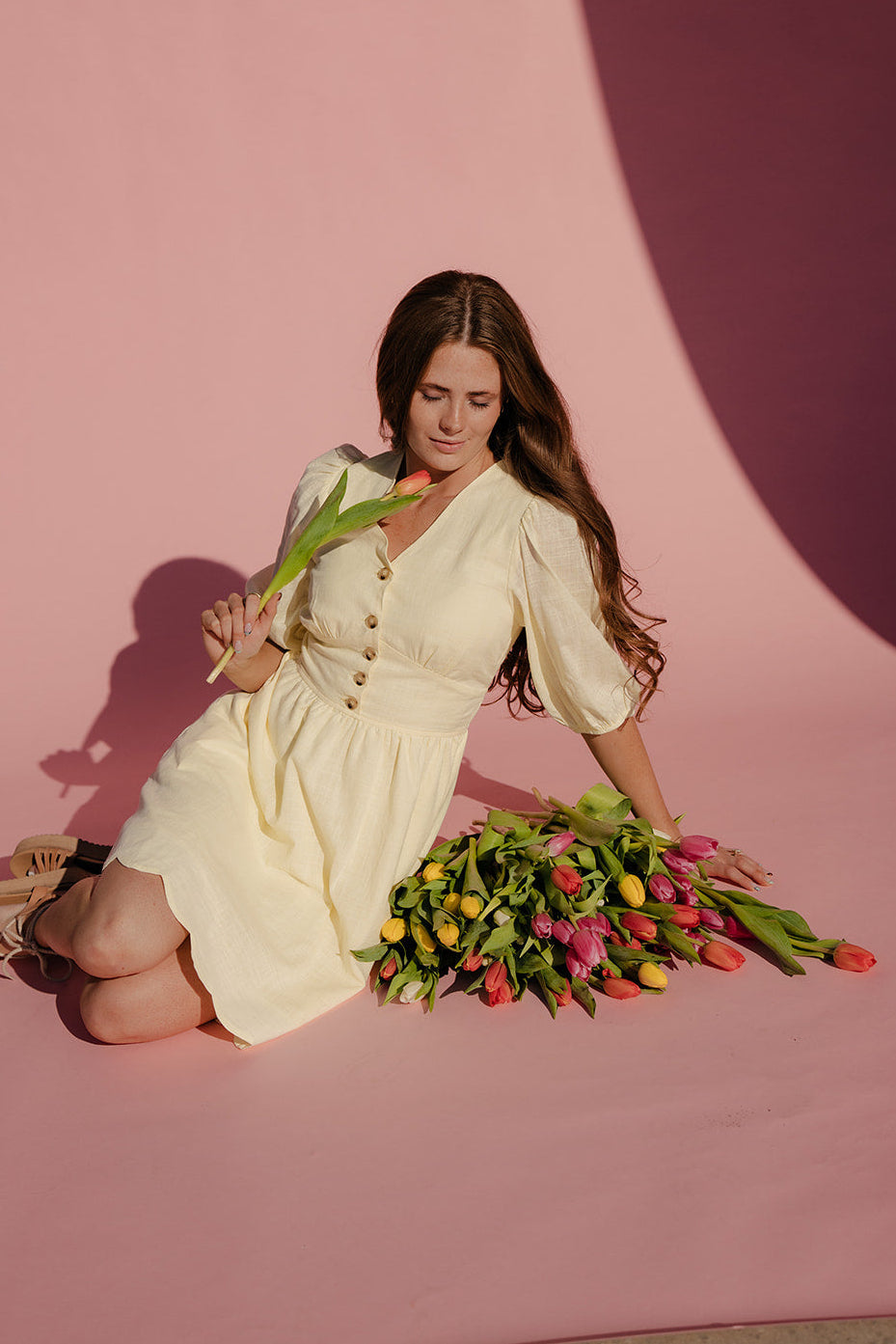 Woman in a white dress holding tulips on a pink background