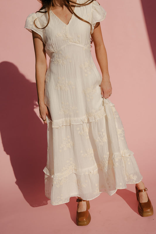 Woman wearing a white dress with ruffled sleeves against a pink background