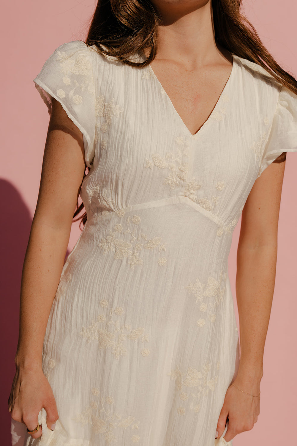 Woman wearing a white floral dress against a pink background