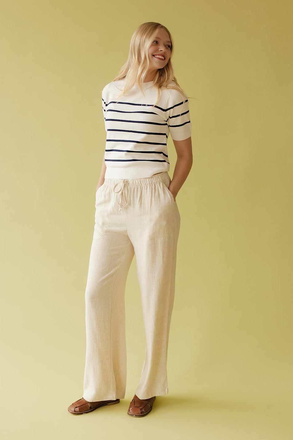 Woman wearing a striped shirt and wide-leg pants against a yellow background
