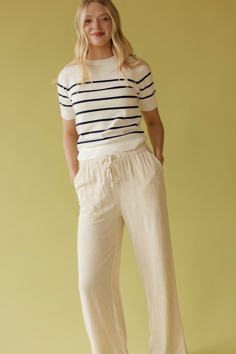 Woman wearing a striped shirt and beige pants against a yellow background