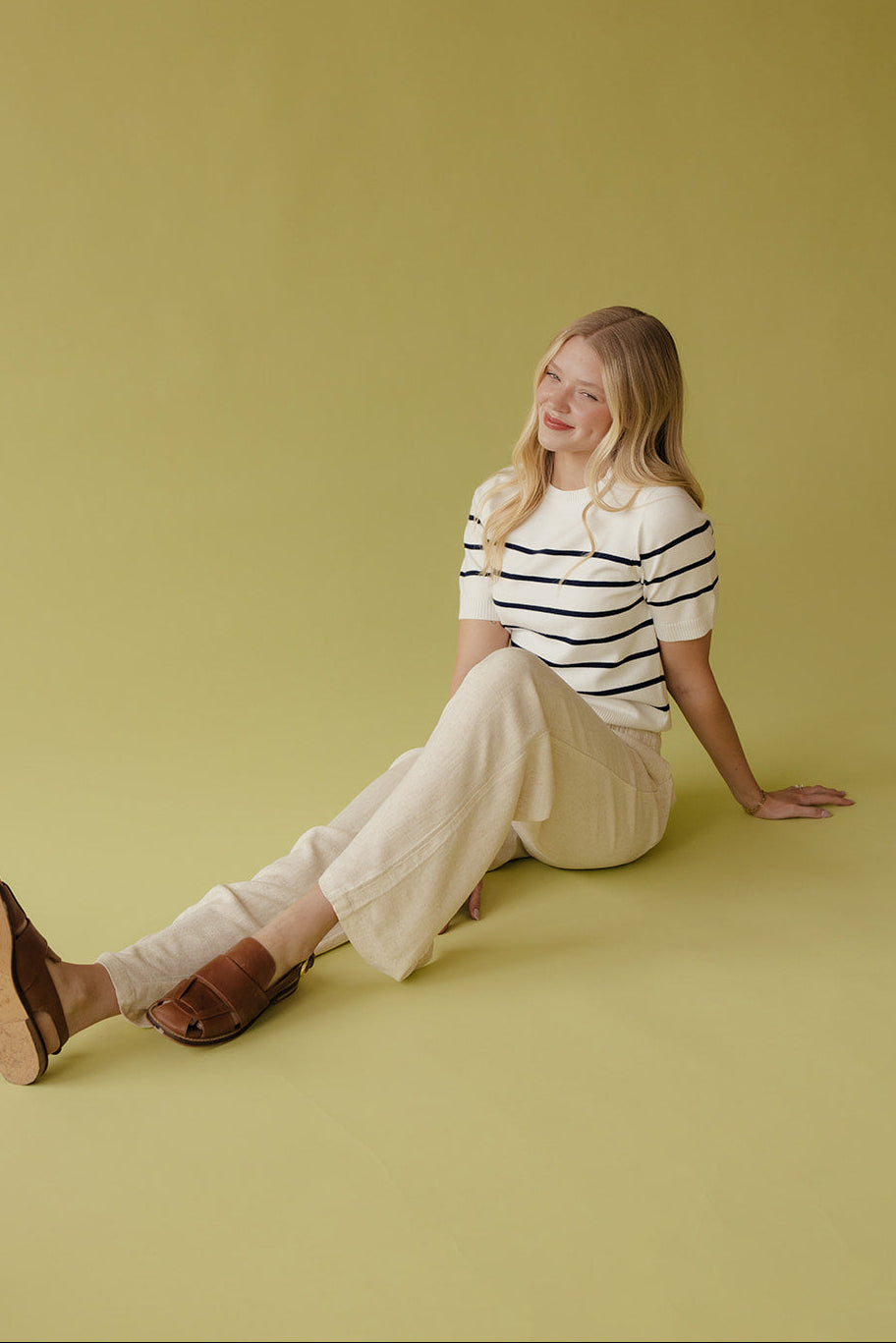 Woman sitting on a yellow floor wearing a striped shirt and white pants.