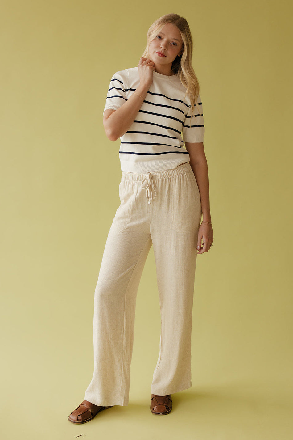 Woman wearing a striped shirt and beige pants against a yellow background