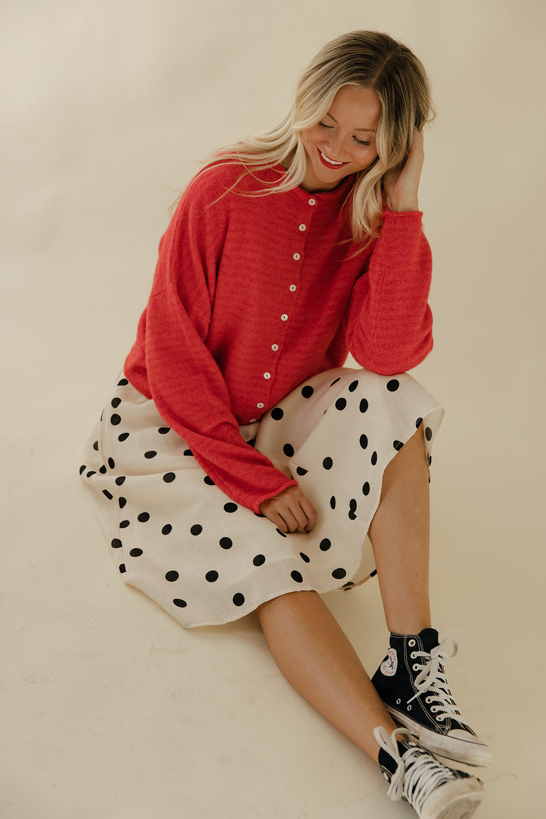 Woman wearing a red sweater and polka dot skirt with high-top sneakers on a plain background