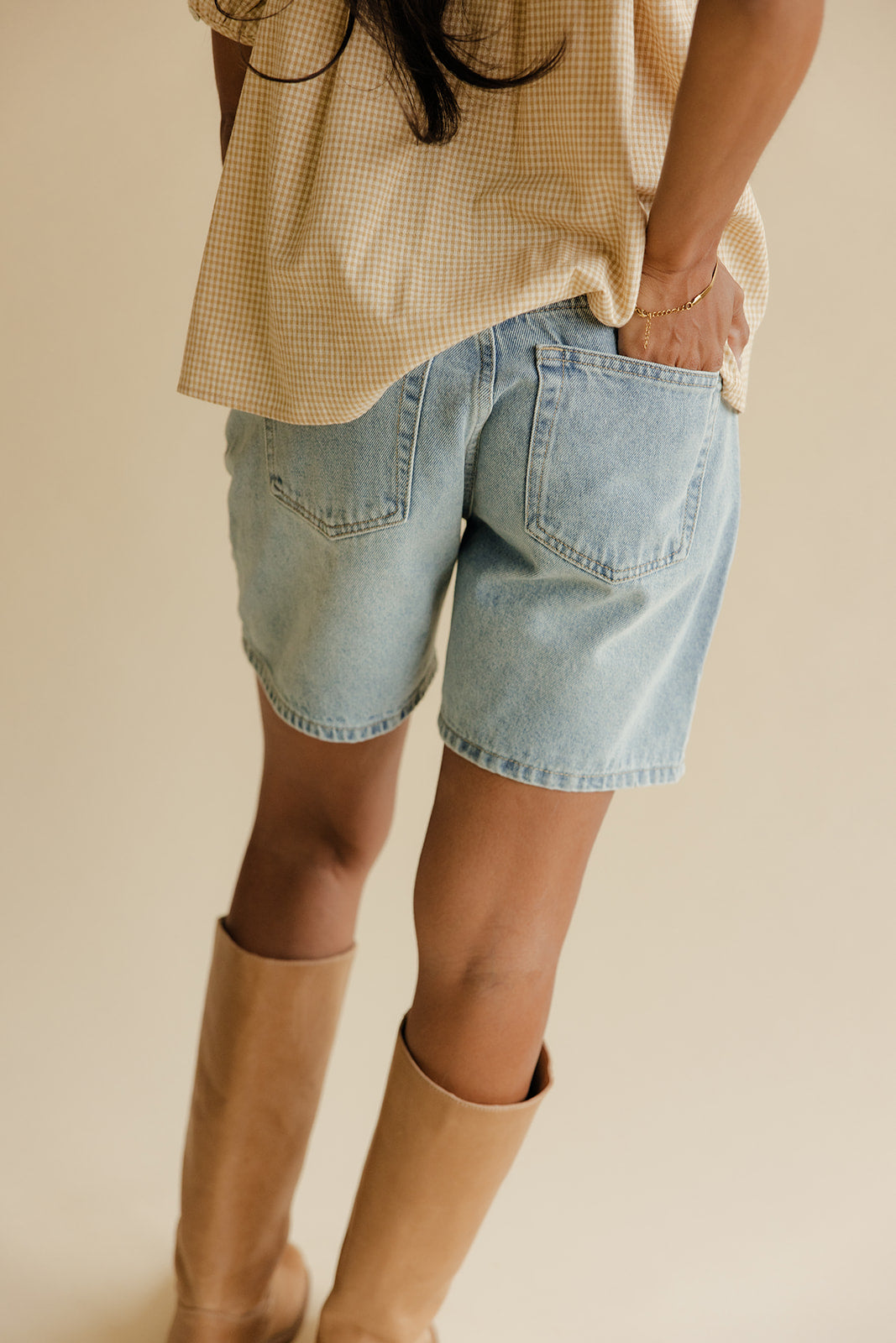 Person wearing a beige checkered shirt, light blue denim shorts, and tan knee-high boots on a neutral background