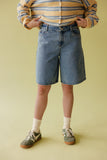 Person wearing a striped sweater, denim shorts, and sneakers on a yellow background