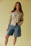 Woman wearing a striped shirt and denim shorts against a yellow background