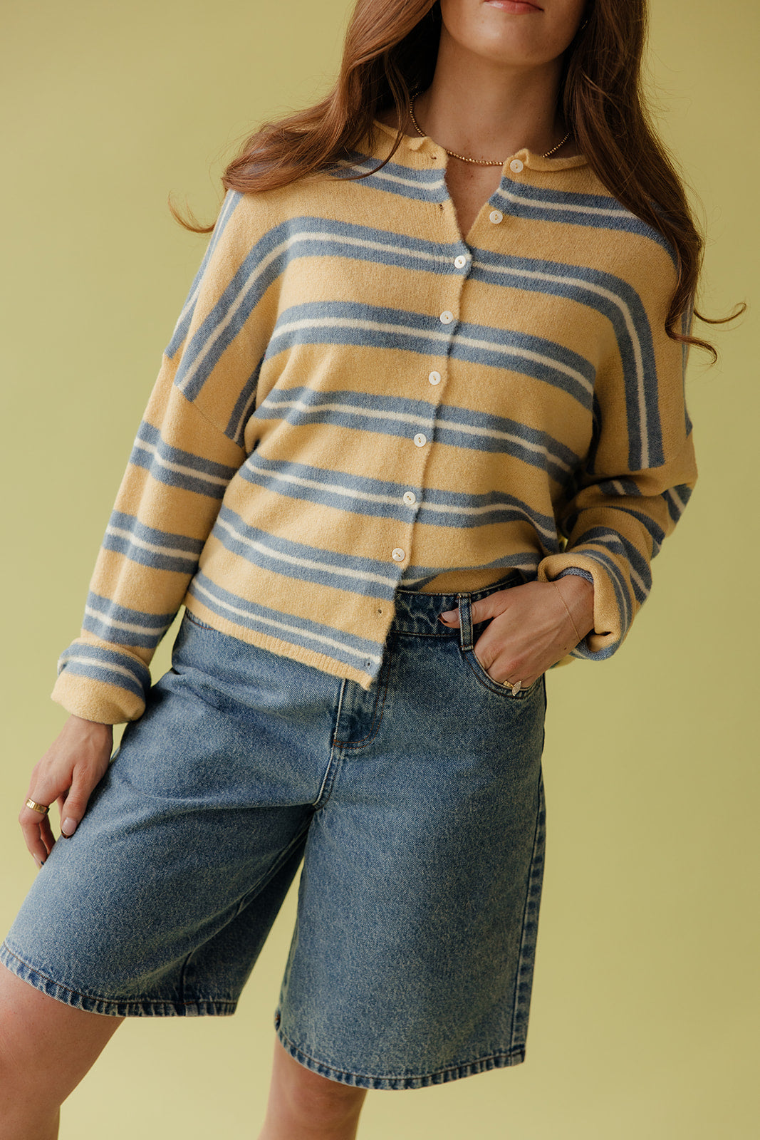 Person wearing a yellow and blue striped shirt with denim shorts on a yellow background