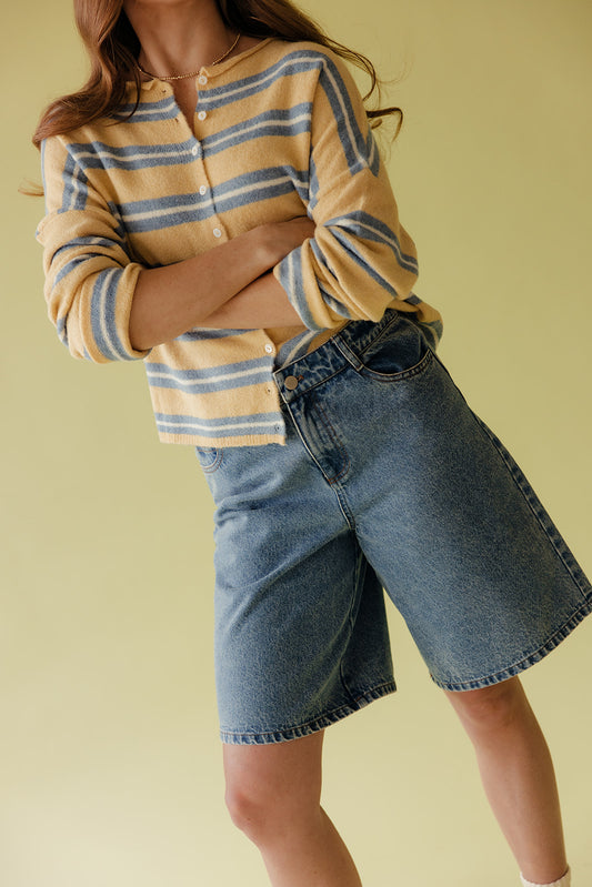 Person wearing a striped shirt and denim shorts on a yellow background