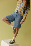 Person wearing a striped shirt, denim skirt, and green shoes on a yellow background