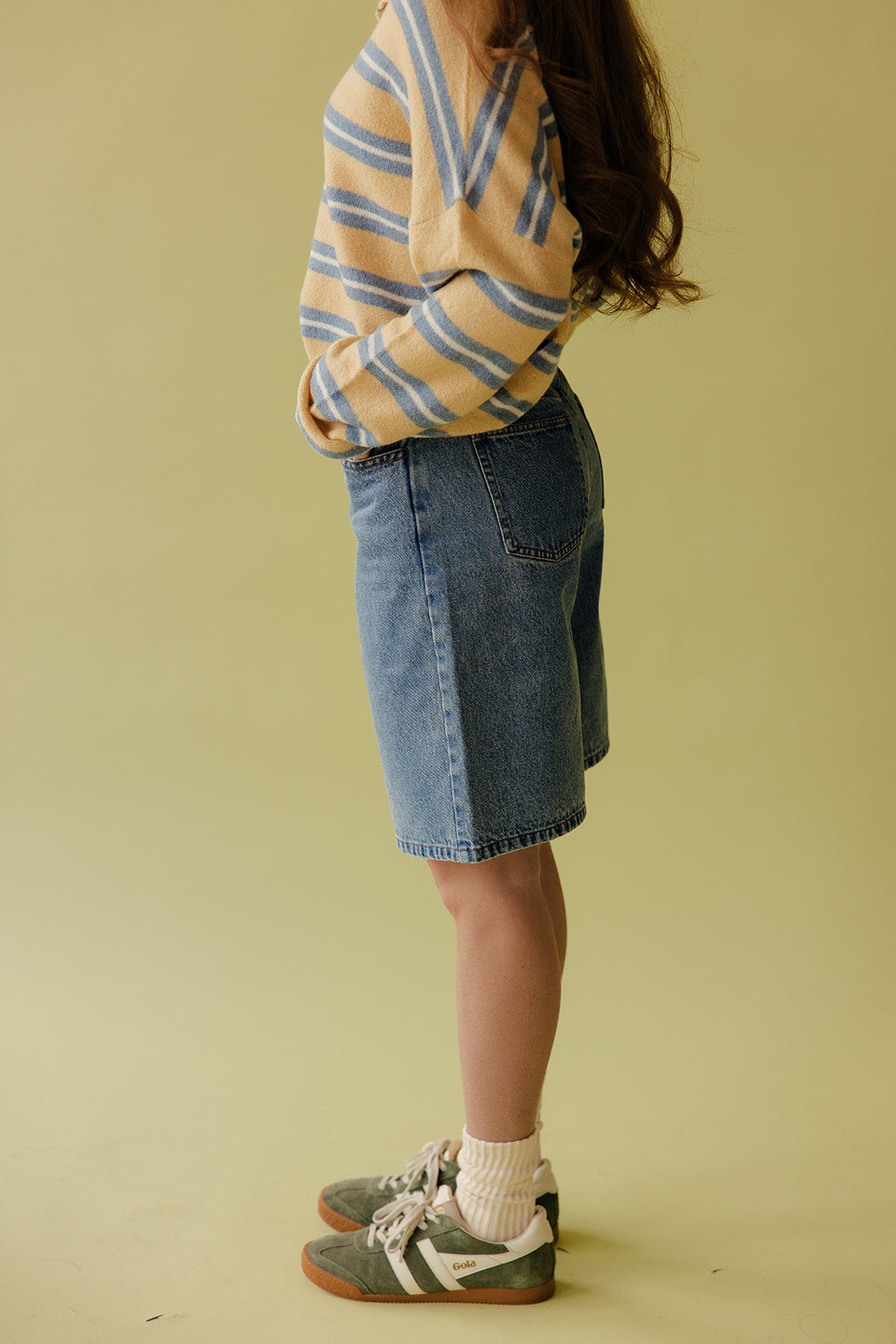 Person wearing a striped sweater and denim skirt on a plain background