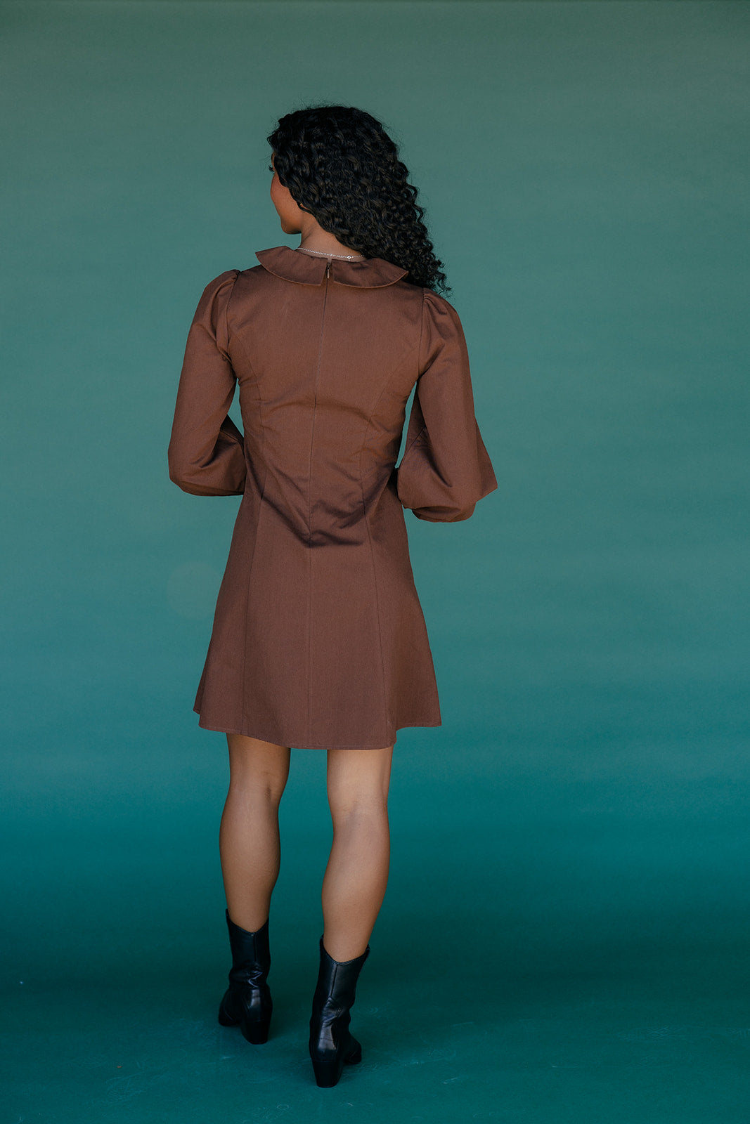 Woman wearing a brown dress against a teal background