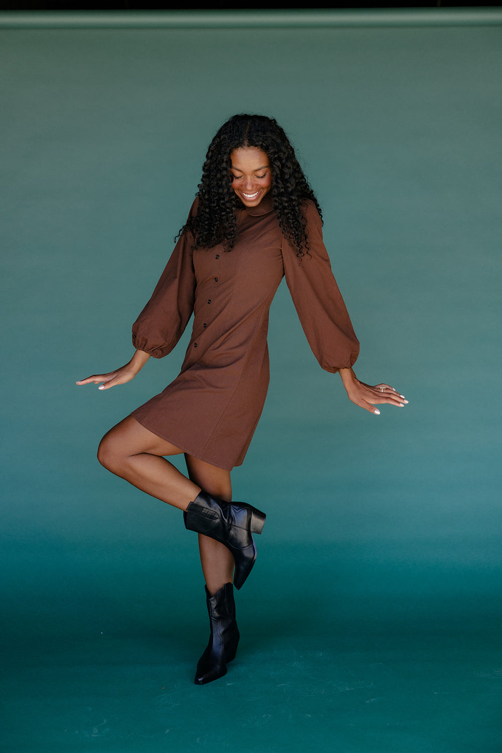 Woman in a brown dress posing against a teal background