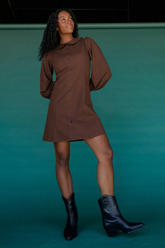Woman wearing a brown dress and black boots against a teal background