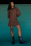Woman wearing a brown dress and black boots against a teal background