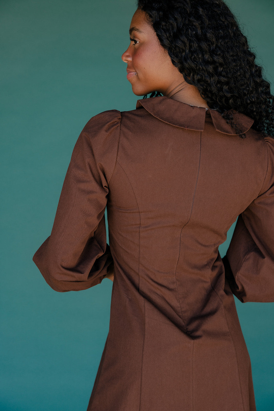 Woman wearing a brown dress against a teal background
