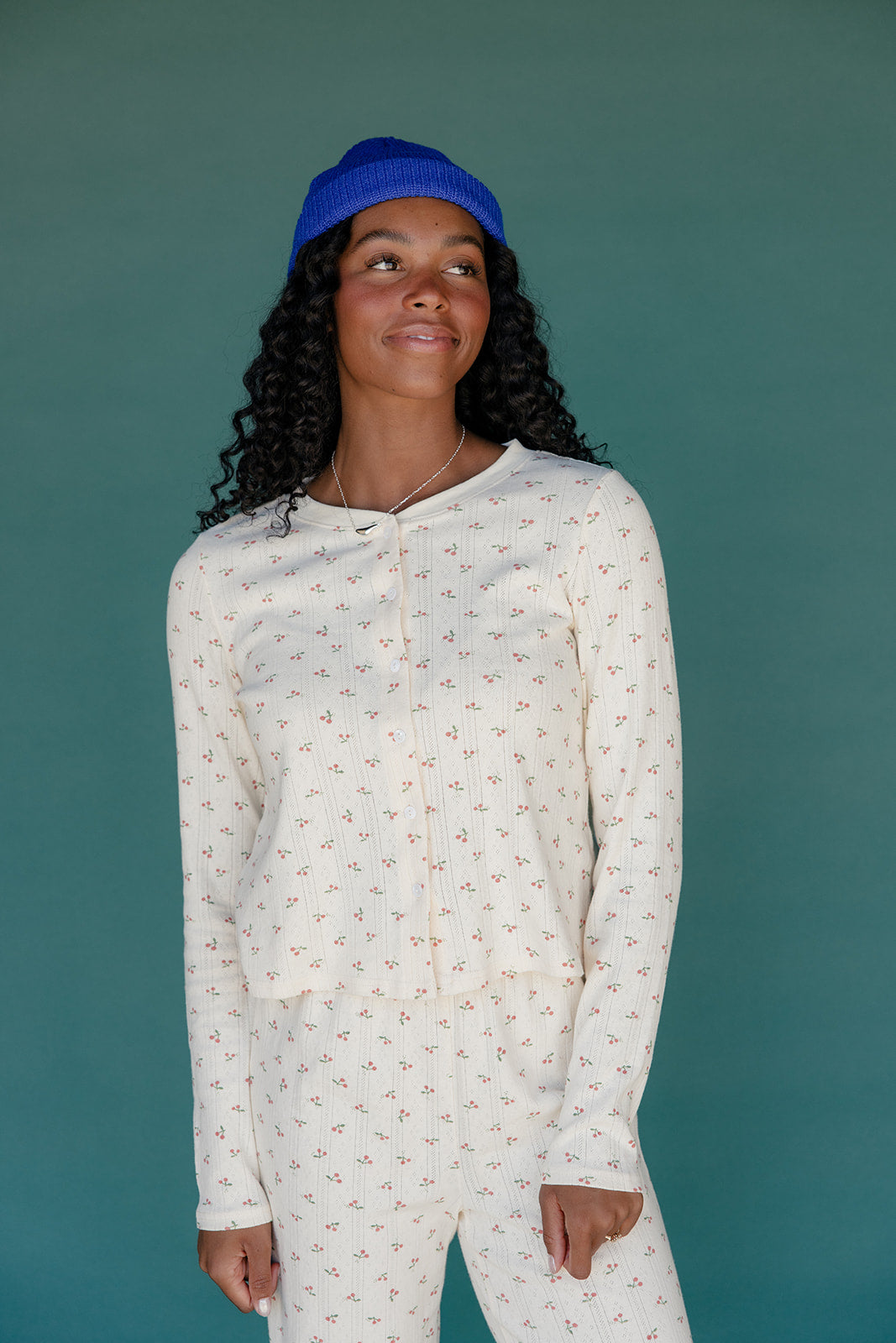 Woman wearing a white patterned onesie with a blue cap against a teal background