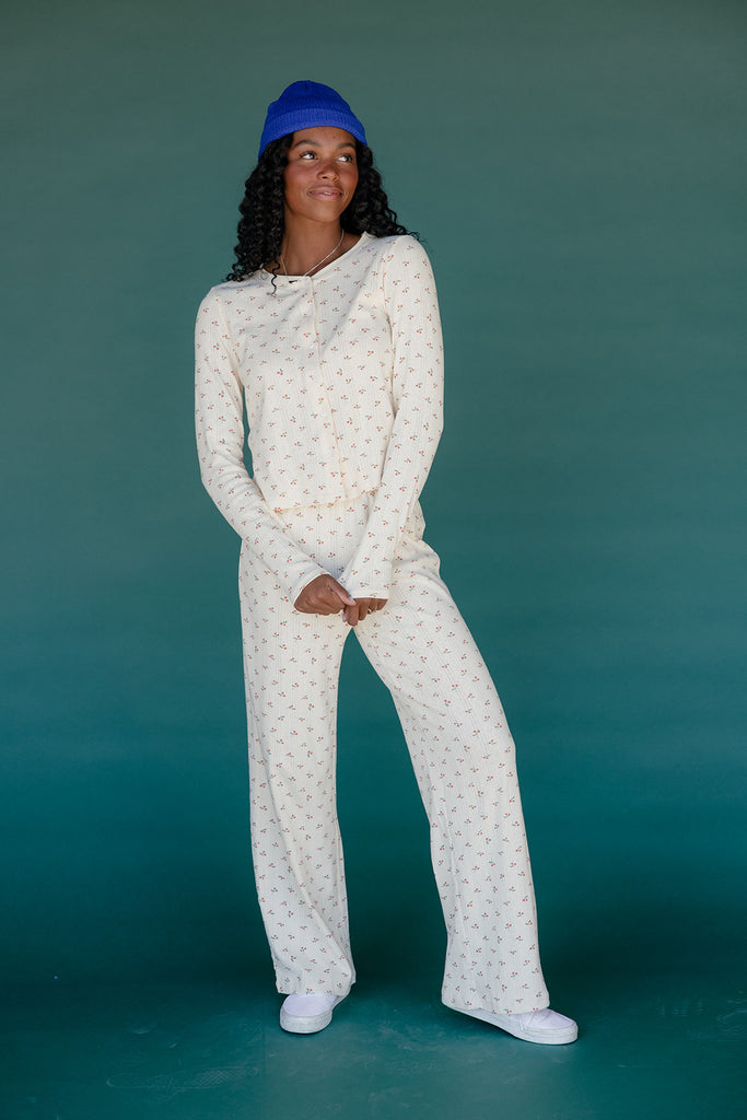 Person wearing a white patterned outfit and blue beanie against a teal background