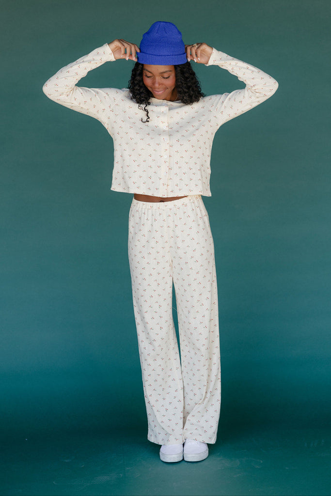 Person wearing a white patterned outfit with a blue beanie against a teal background