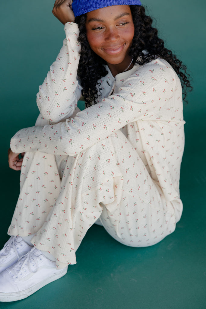 Person wearing a white floral outfit with a blue beanie against a teal background