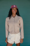 Woman wearing a beige button-up shirt and white shorts with a maroon cap against a teal background